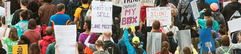 Crowd of protesters holding up signs with various messages at a rally.