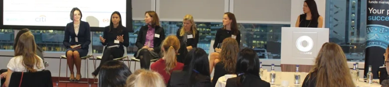Panel of female professionals speaking at an investment banking event with audience in foreground.