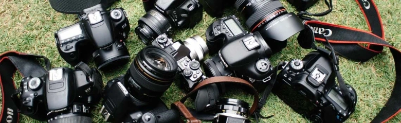 Assortment of professional cameras and lenses on grass, representing press photography equipment.