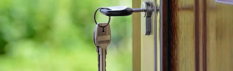 A key inserted into a door lock. There is another key hanging from the inserted one attached by a keyring.