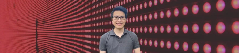 Smiling person with glasses standing in front of a red digital dot matrix display.