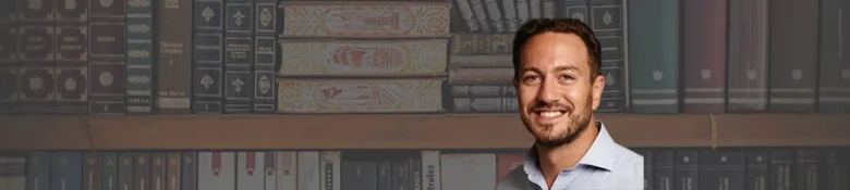Smiling man in a blue shirt with a backdrop of bookshelves filled with legal texts.