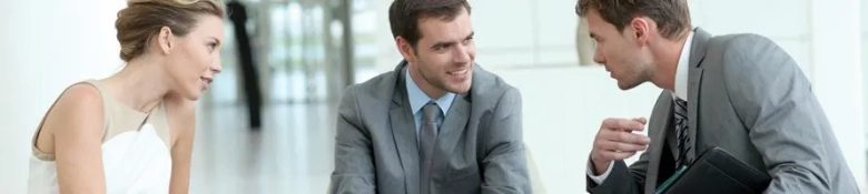 Two men in business attire engaged in conversation with a woman in a white dress, possibly during a consultation.