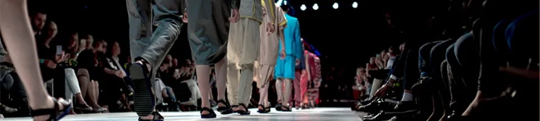 Models walking on runway during a fashion show with audience in background.