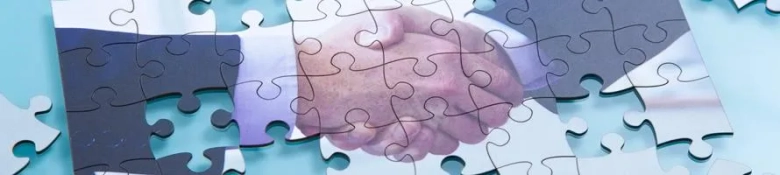 Handshake between two people superimposed on jigsaw puzzle pieces, symbolizing consulting collaboration.