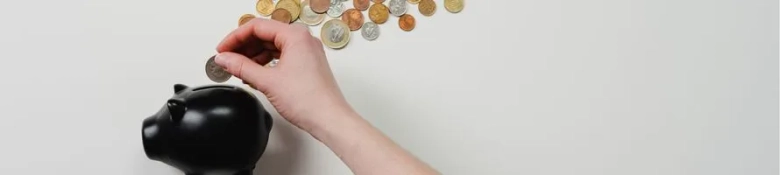 A hand inserting a coin into a black piggy bank.