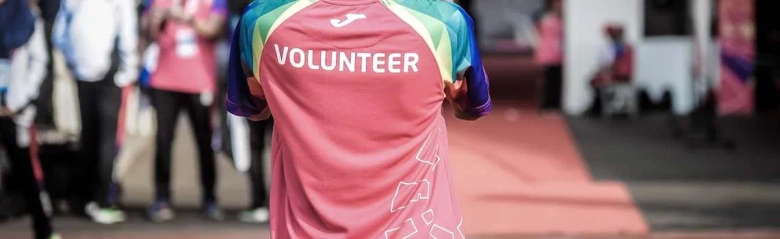 Person wearing a pink 'VOLUNTEER' t-shirt at an event, viewed from behind.