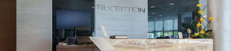 Modern hotel reception desk with computers and decorative flowers.