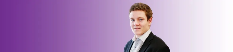Confident young man in business attire with a slight smile against a purple gradient background.