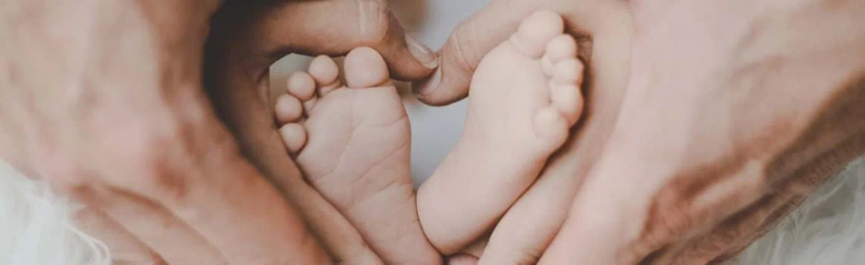 Adult hands cradling a pair of newborn baby feet in a heart shape.