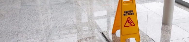 Yellow caution sign warning of wet floor on a shiny tiled surface.