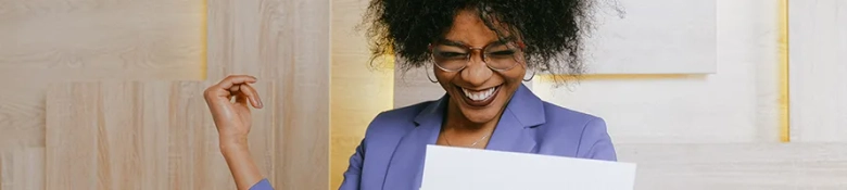 A woman smiling while holding and looking at a sheet of paper.