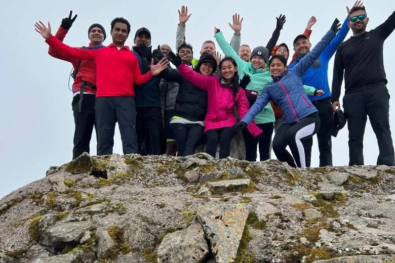 A group of people smiling stood on top of a mountain 