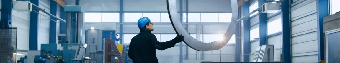 Engineer in hard hat inspecting a large curved metal component in an industrial manufacturing facility.