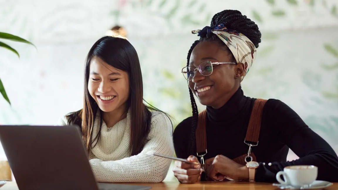 two women working on a laptop smiling