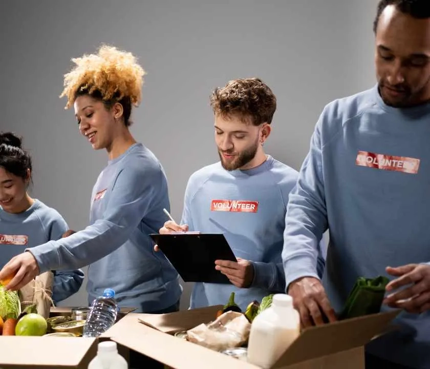 A collection of volunteers wearing Tshirts saying 'volunteers' packing food boxes