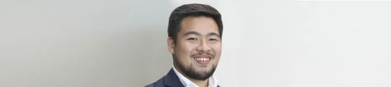 Smiling young man in business attire against a neutral background.