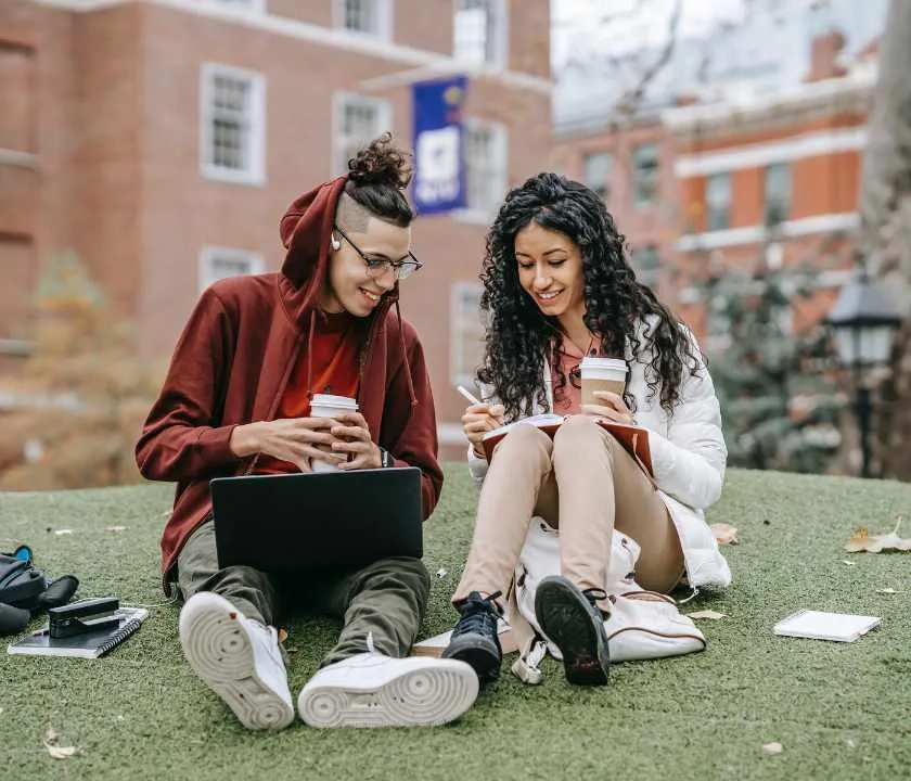 Two students sat on the grass outside a university building