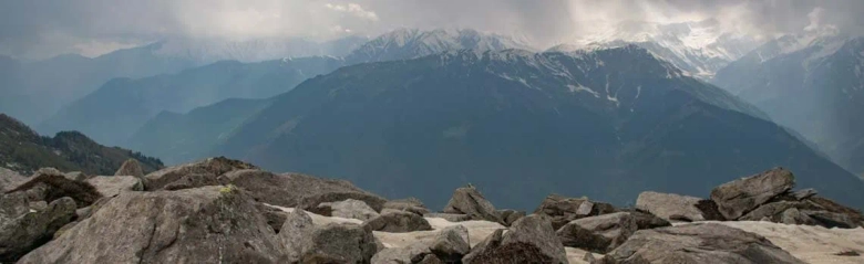 Panoramic view of a mountain range with snow-capped peaks behind rocky foreground.