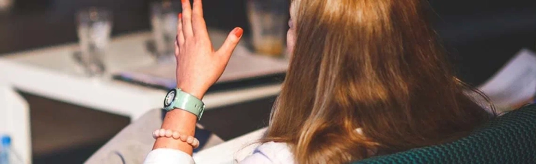 Student raising hand in a classroom setting to ask a question.