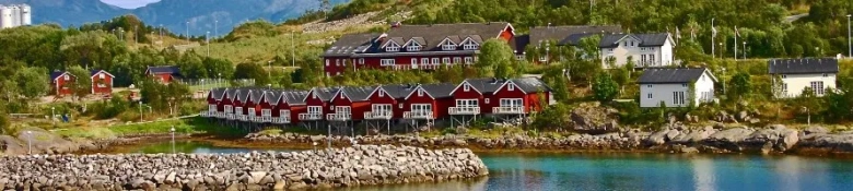 A row of red houses on the shore of a sea inlet in Norway.