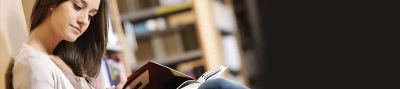 Student reading a book in a library, symbolizing academic engagement and learning.