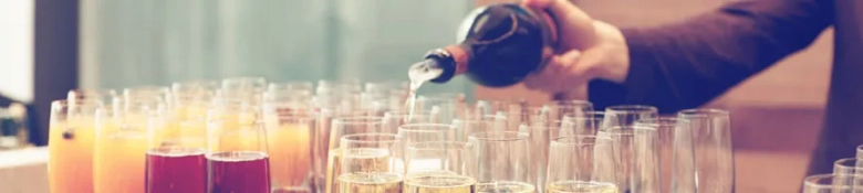 Bartender pouring various drinks into glasses arranged on a bar counter.