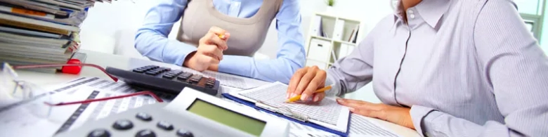 Two professionals working with financial documents and a calculator on a desk.