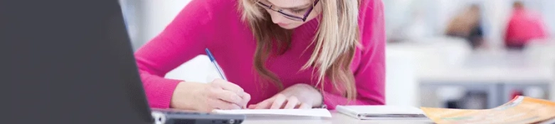 Girl in pink jumper writing in a notepad with a pen