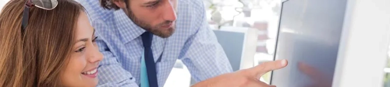 Two professionals collaborating over a computer screen in an office setting.