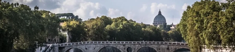 A view of a cathedral in Italy standing behind trees and a bridge.