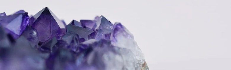Close-up of vibrant purple amethyst crystal points against a white background.