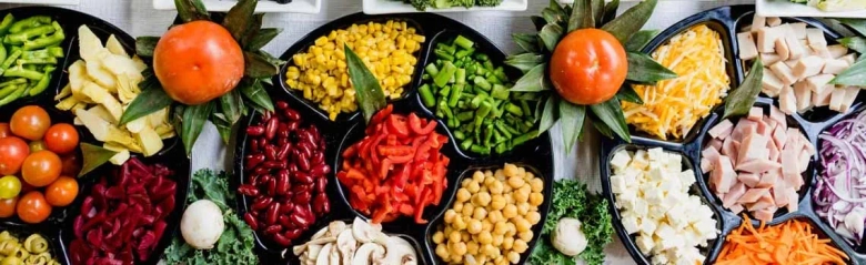 Assorted fresh vegetables and legumes neatly arranged in black bowls on a table.