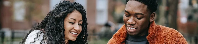 Two university students smiling whilst they swap notes