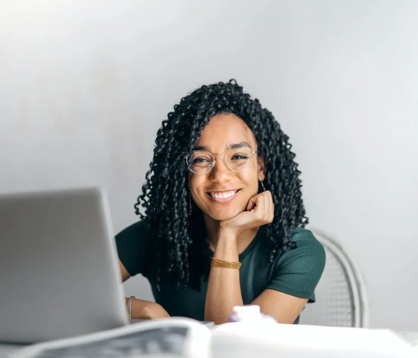 A woman smiling at the camera. There is a laptop in front of her.  