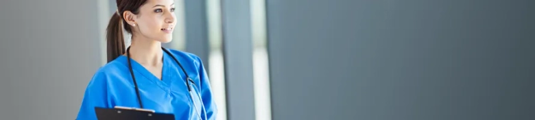 Confident nurse in blue scrubs with a stethoscope around her neck holding a clipboard.