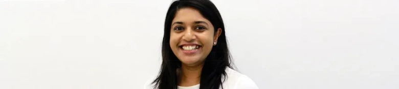 Smiling woman with dark hair against a white background, conveying a positive work environment.