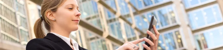 Young professional woman using smartphone with office buildings in the background.