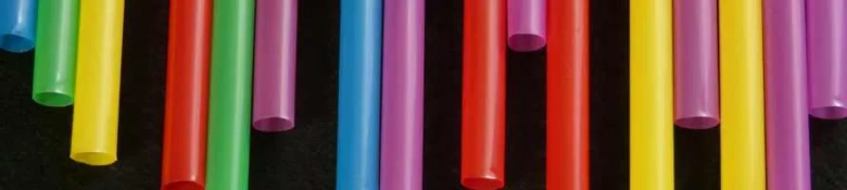 Multiple, brightly coloured plastic straws set against a black background