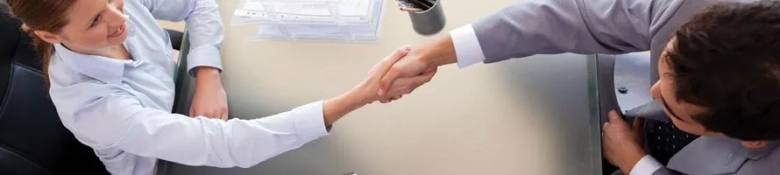 Overhead view of two professionals shaking hands over a desk, indicating a successful job interview.