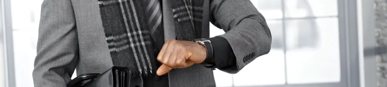 Professional dressed in a plaid blazer checking the time on their wristwatch while holding a briefcase.