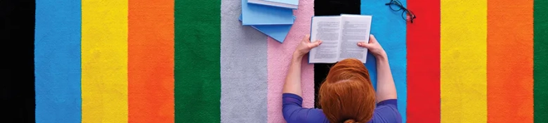 Person reading a book against a colorful striped background.