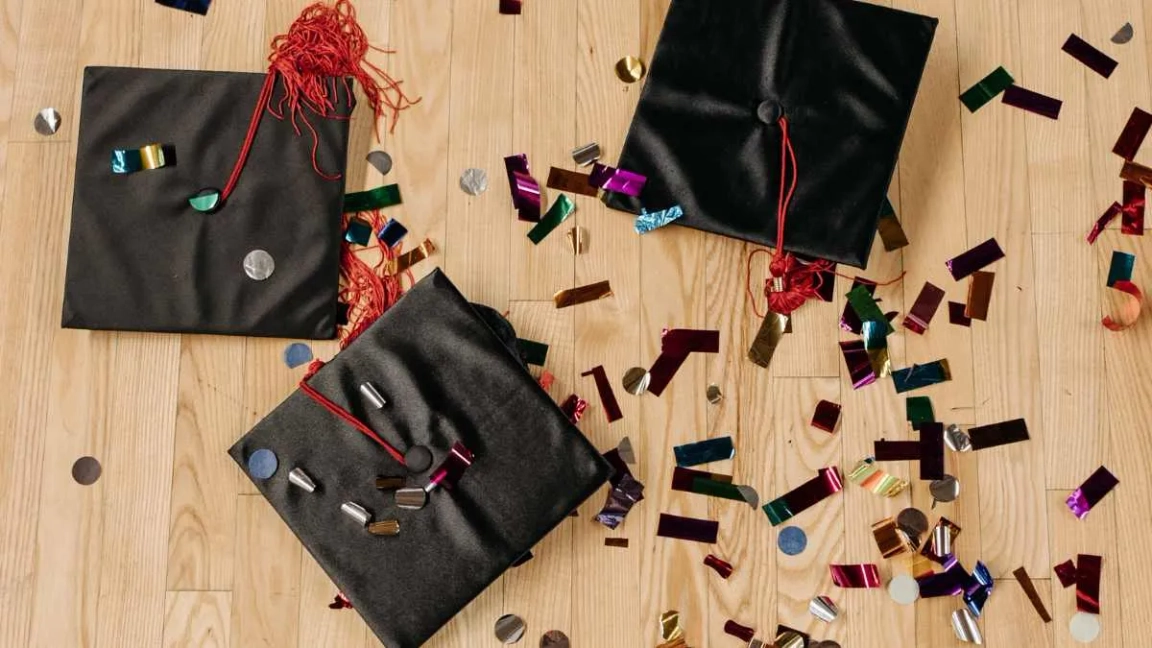 Mortarboards on a wooden floor surrounded by celebratory confetti