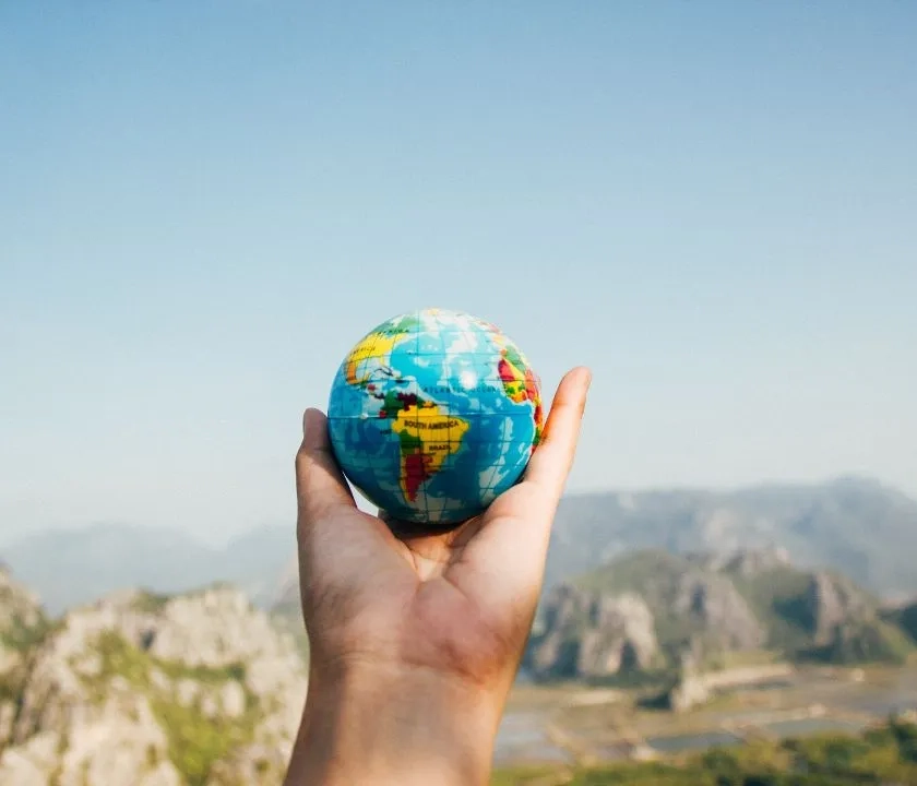 an outstretched hand holding a small planet Earth globe. There are mountains in the background. 