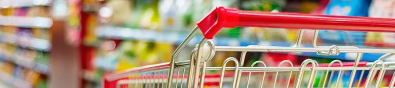 Close-up of an empty shopping cart in a store aisle with blurred products on shelves in the background.