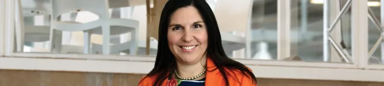 Professional woman in an orange blazer smiling confidently in an office environment.