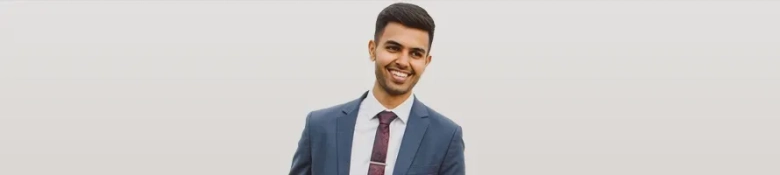 Confident young professional in a suit with a tie smiling against a light background.