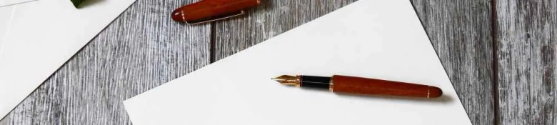 An elegant fountain pen resting on top of writing paper on a wooden desk surface