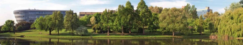 Scenic view of University of Surrey campus with modern buildings and lush greenery reflected in a lake.