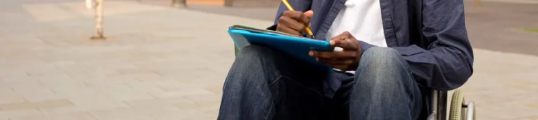 The picture shows a person writing their CV on a clipboard sitting outside. 